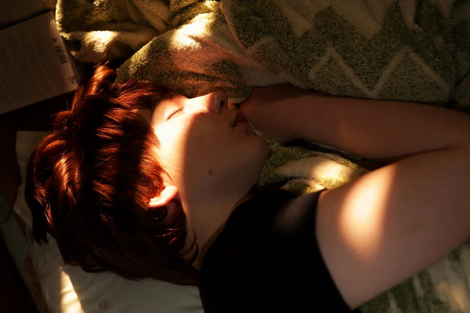 Young boy sleeping soundly in bed as a bright ray of morning sunlight warms his face.